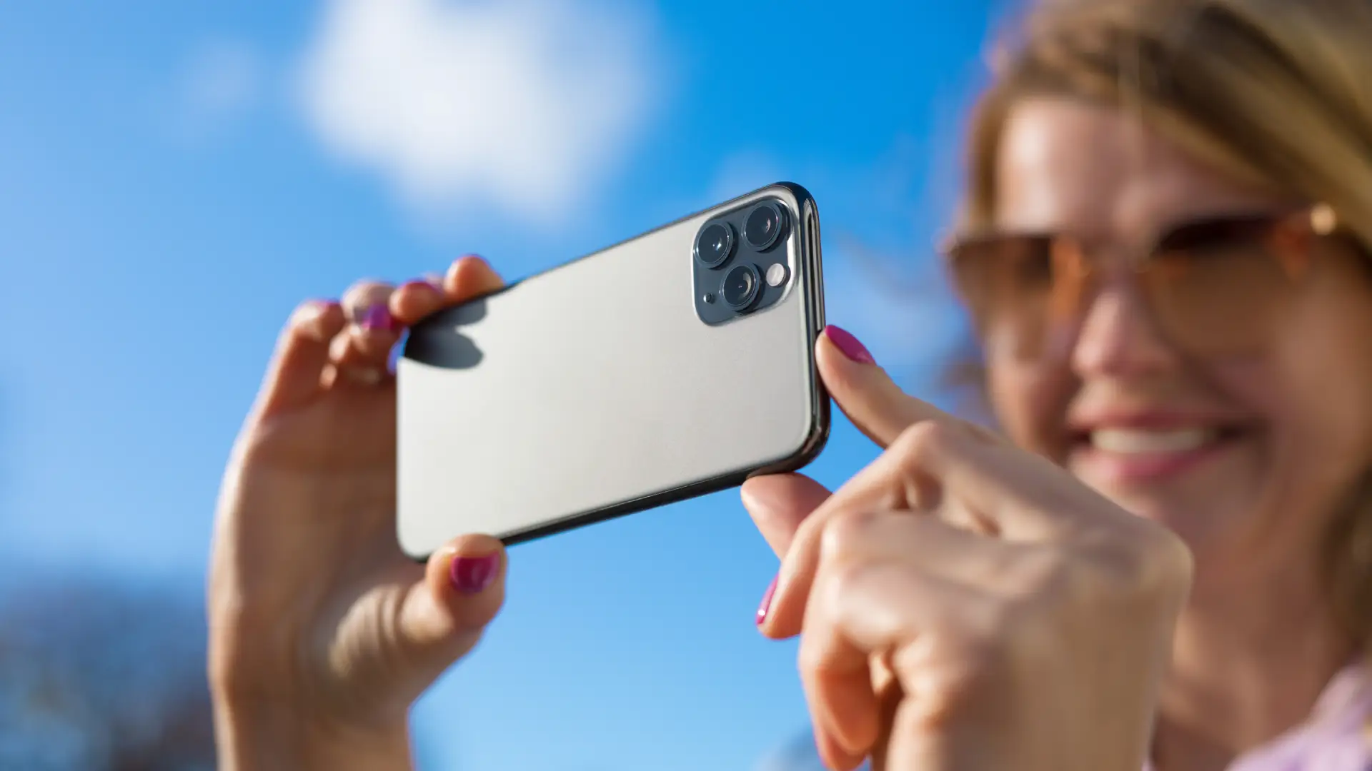 Uma mulher sorri enquanto aponta o celular para o seu rosto para tirar uma foto
