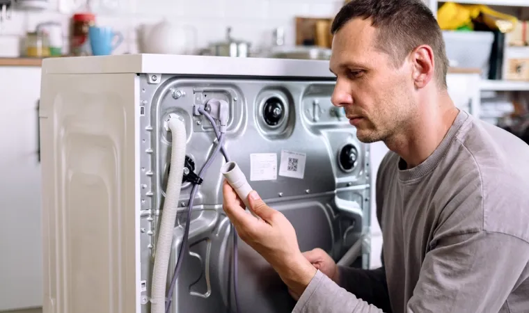 Homem segurando um cano de água atrás de uma máquina de lavar branca.