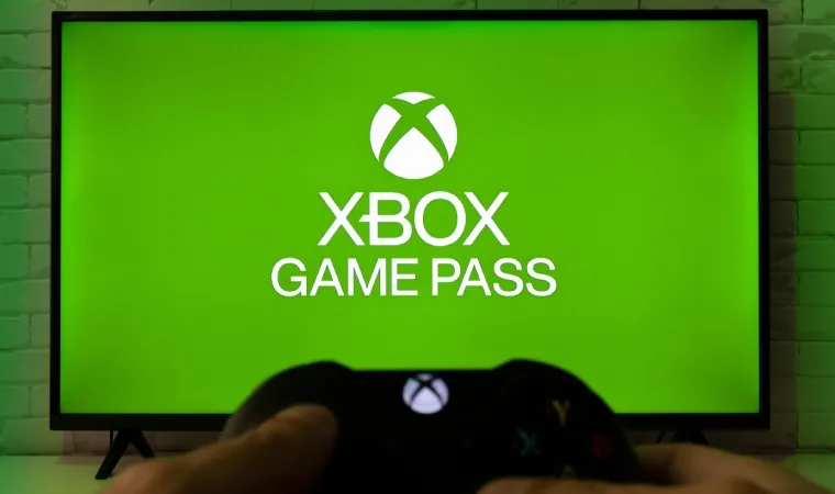 Imagem de duas mãos segurando um controle de videogame na frente de uma Tv com a logo do Xbox Game Pass
