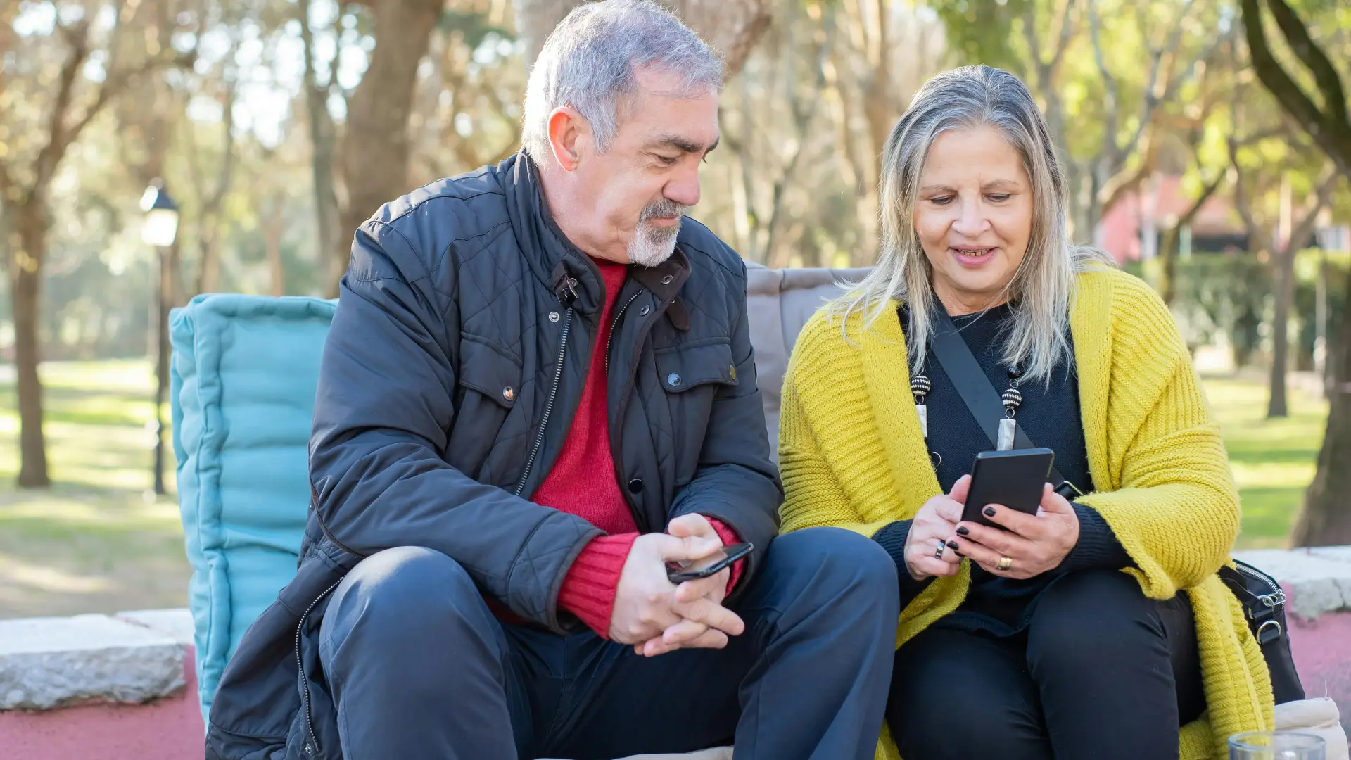 Duas pessoas estão sentadas em um banco olhando para um celular