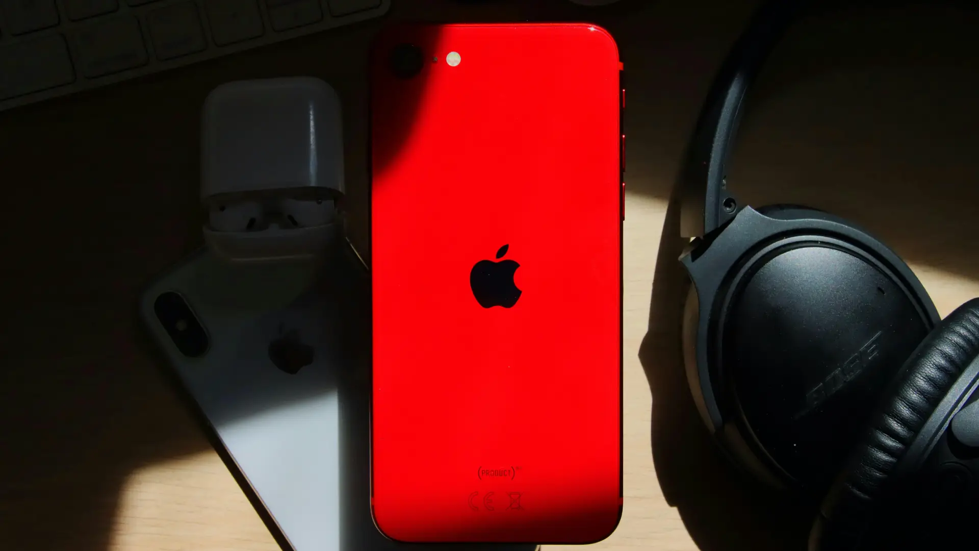 Um celular de cor vermelha está ao lado de alguns acessórios sobre a mesa