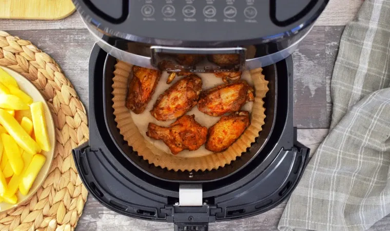 Visão de cima de uma air fryer preta aberta com pedaços de frango grelhados dentro do cesto.