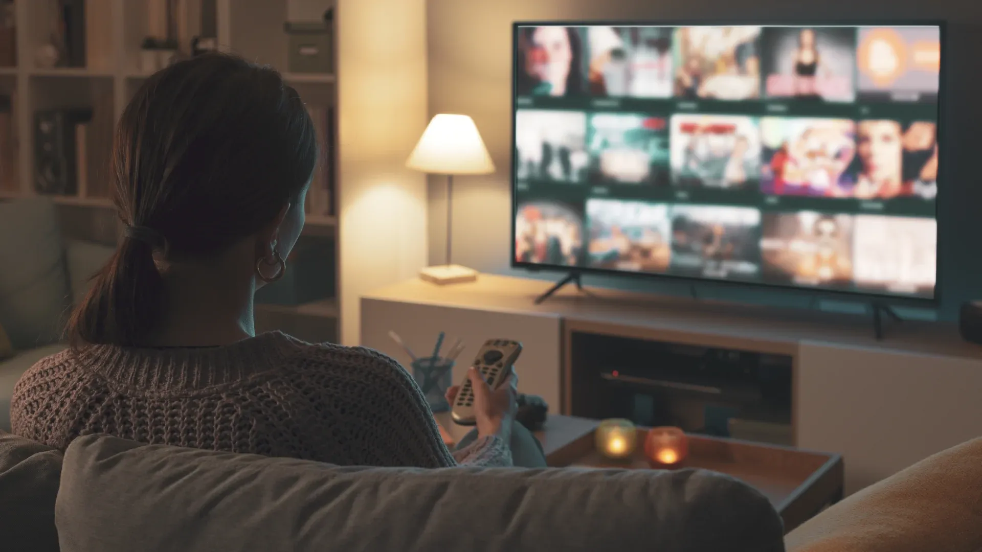 Mulher assistindo TV na sala de estar, em um ambiente escuro. 