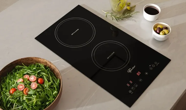 Cooktop por indução da Fischer em cima de uma bancada ao lado de uma tigela de saladas e potes com temperos.