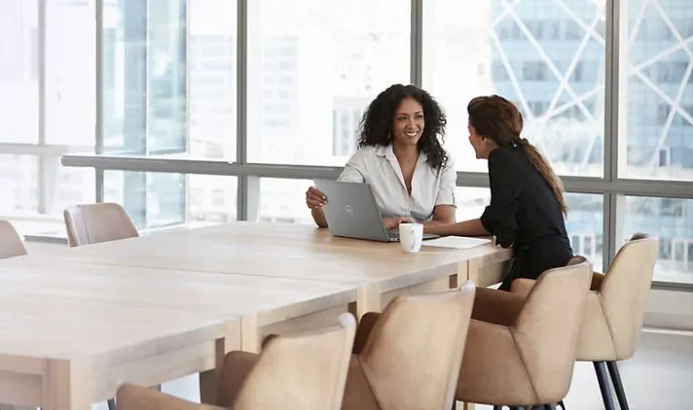 Mulheres em uma mesa de reuniões de escritório elegante conversam em frente a um notebook Dell Latitude