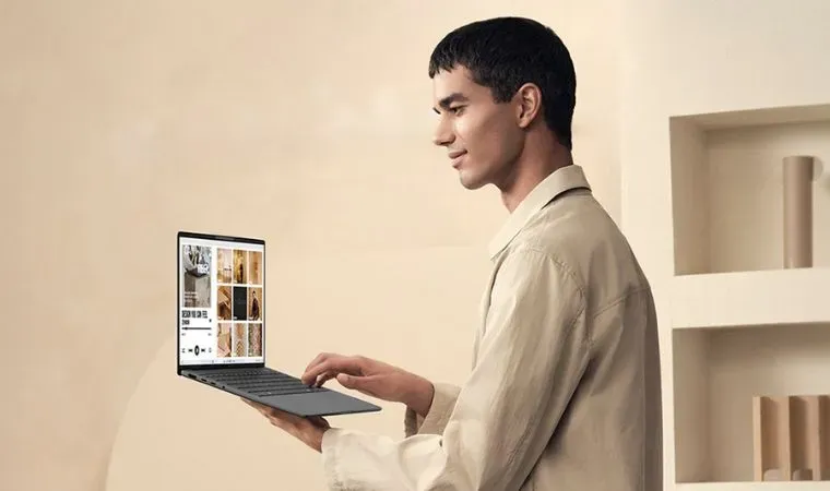 Homem jovem segura notebook Asus a14 leve e compacto em uma mão enquanto digita com a outra