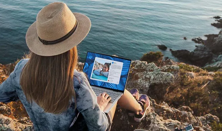 Mulher sentada em rochedo à beira do mar usa um Dell Inspiron 14 2 em 1 para trabalhar 