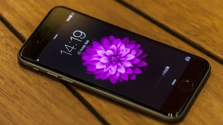 iPhone 6S com tela virada para cima sobre mesa de madeira