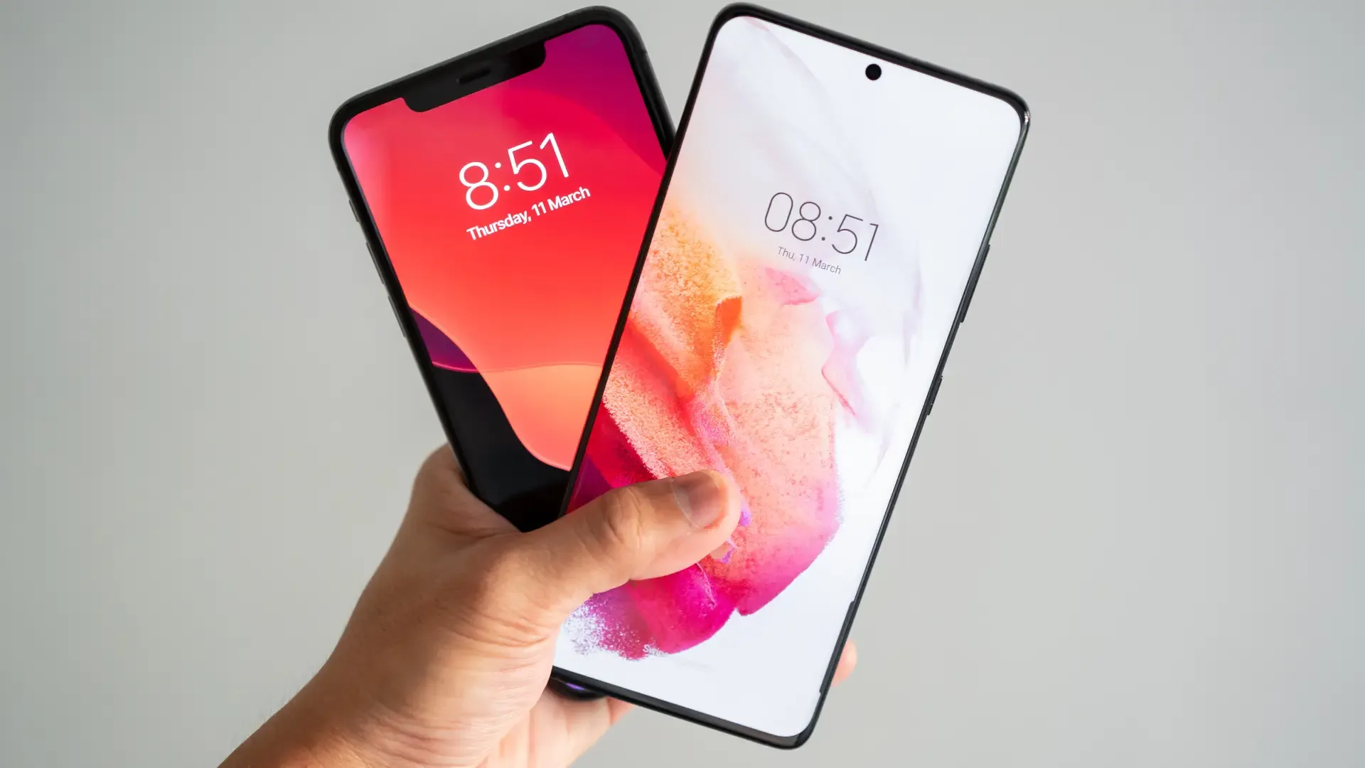 Uma mão masculindo segurando um iPhone e um Samsung Galaxy lado a lado