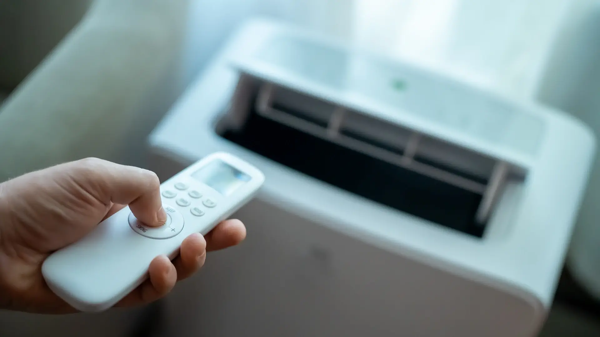 Mão segurando o controle remoto apontando para o ar-condicionado portátil de chão.