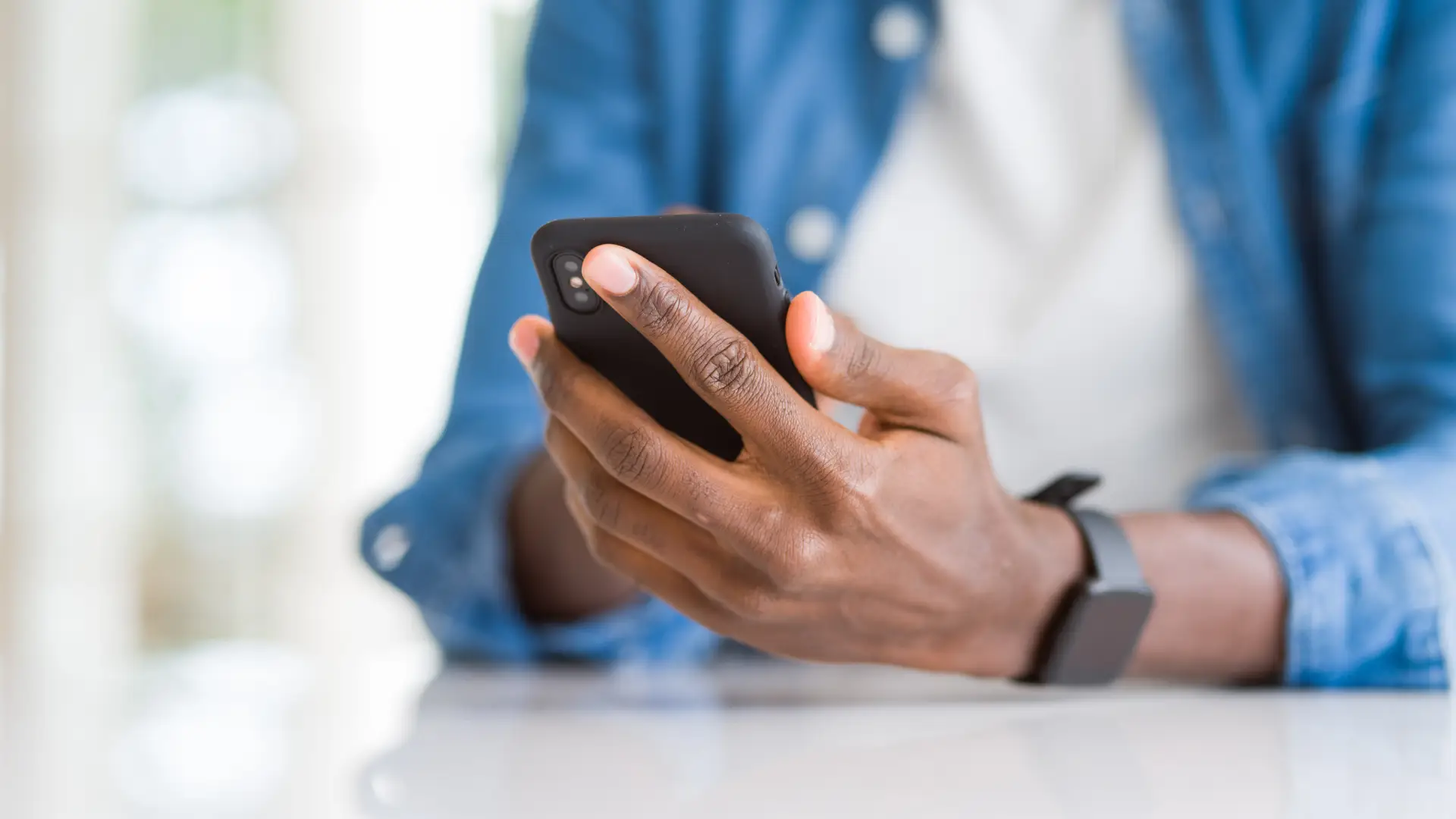 Homem segurando celular preto apoiando braços em uma mesa