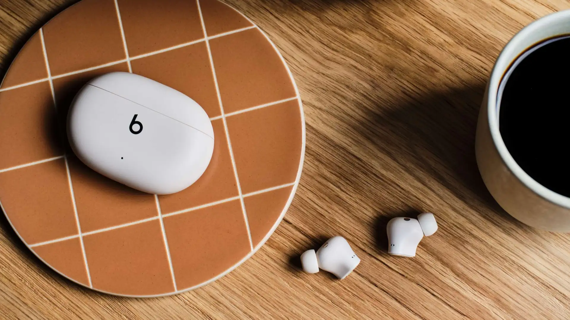 Fone de ouvido Beats sobre um prato marrom ao lado de uma xícara de café