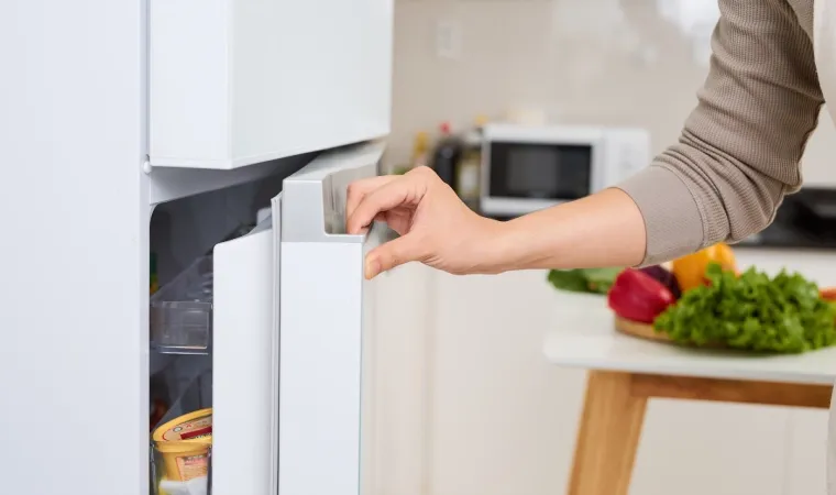 Mulher abrindo uma geladeira pequena branca.