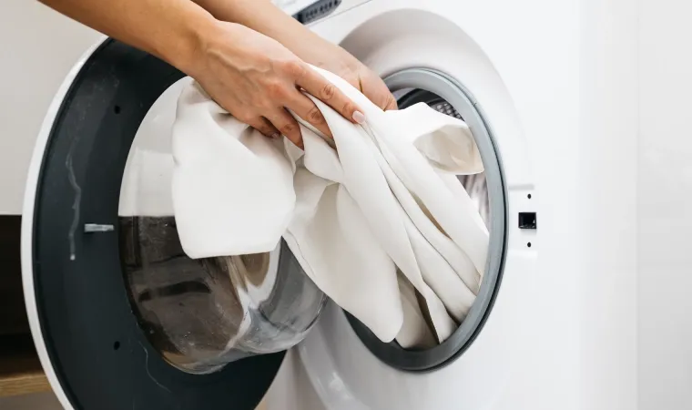 Roupa branca sendo tirada de uma máquina lava e seca.