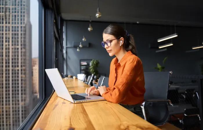 Mulher de óculos com aspecto de satisfeita trabalha em frente a notebook em uma sala elegante 