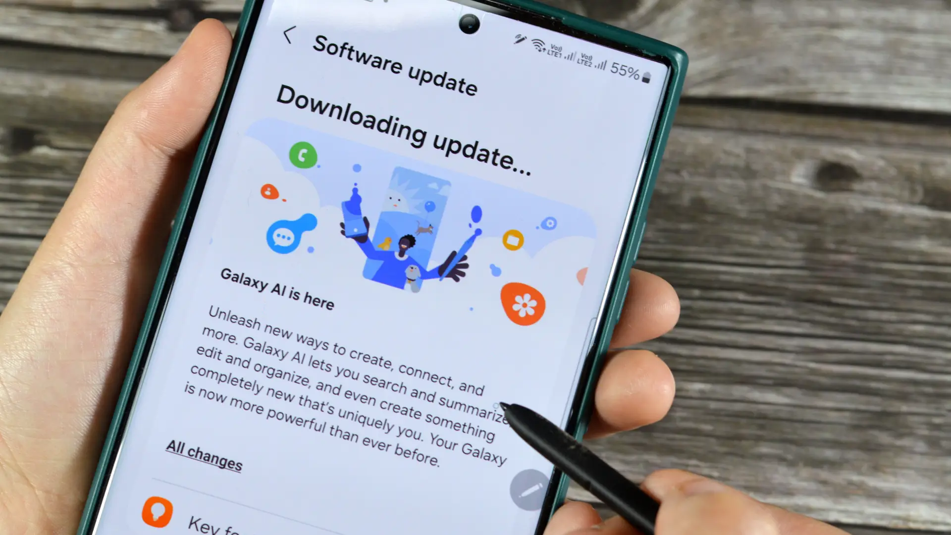 Mão segurando um celular que está sendo atualizado para a One UI 8