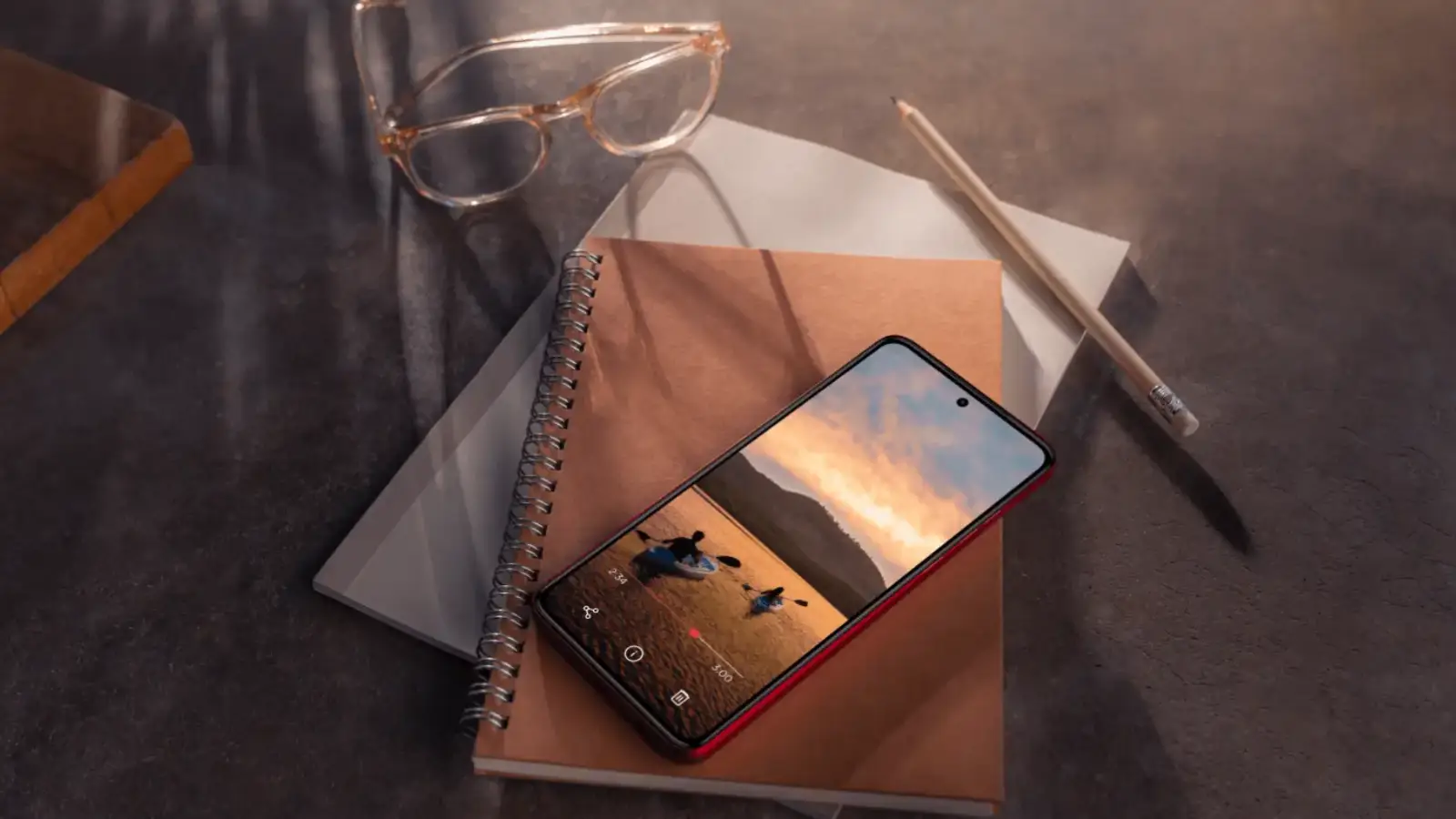 Tela do celular Moto G84 em cima de caderno ao lado de óculos