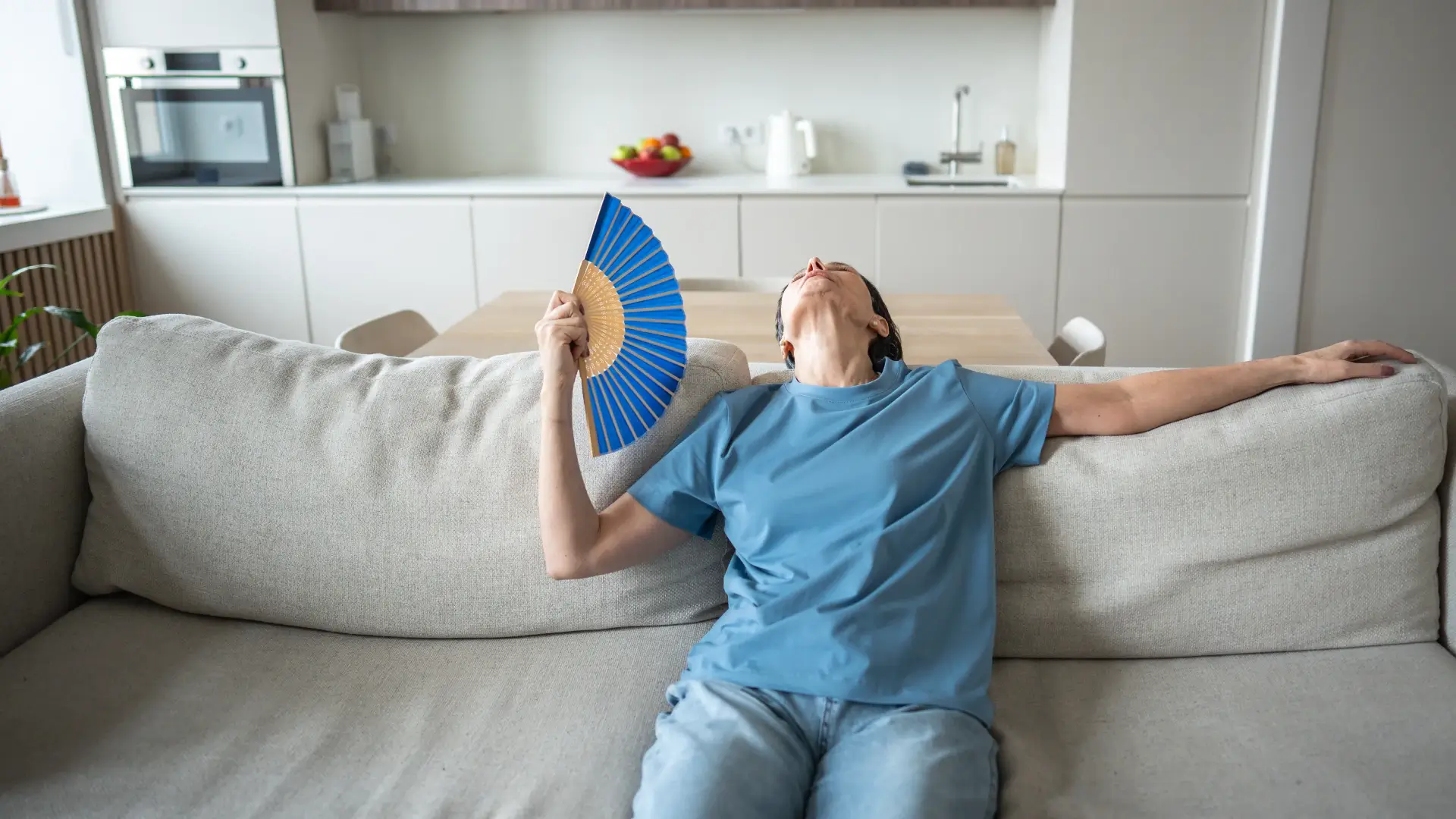 Mulher sentada no sofá se abanando com o leque para espantar o calor 