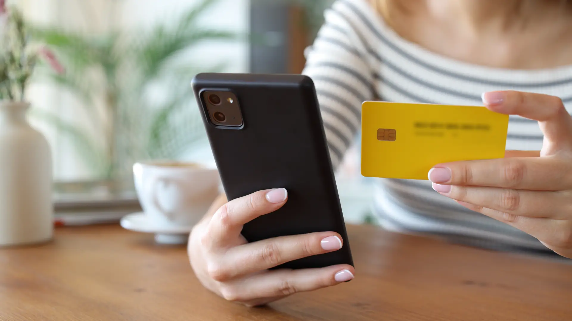 Imagem de uma mulher segurando o celular em uma mão e o cartão de crédito na outra