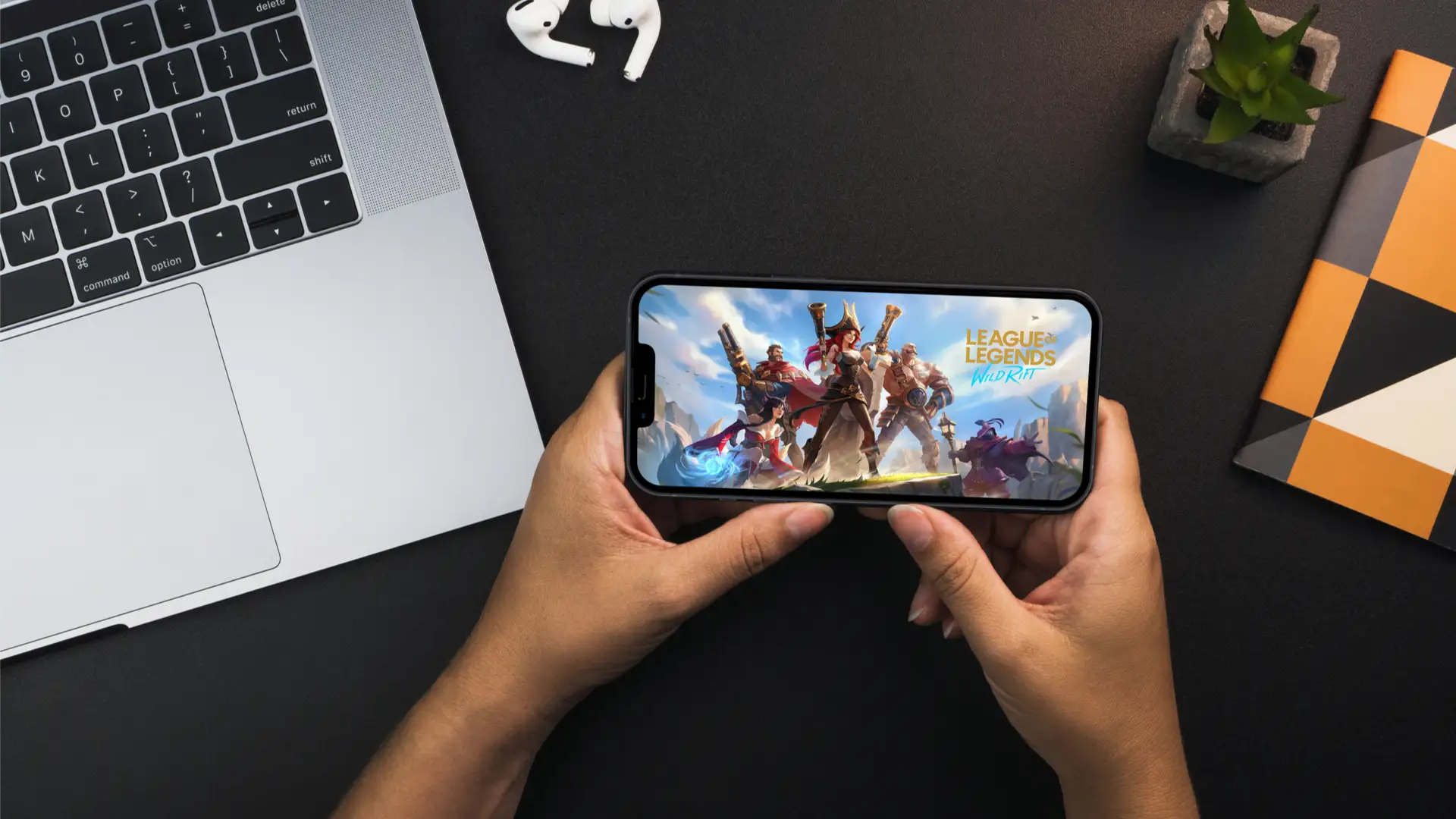 Imagem de duas mãos segurando um celular com o jogo Wild Rift em sua tela