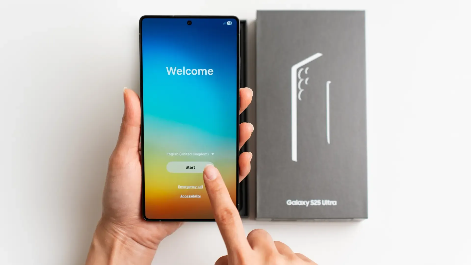 Uma pessoa segura um celular na mão. Sobre uma mesa está a caixa do aparelho 