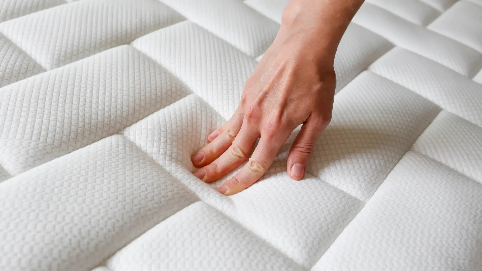 mão tocando e sentindo a maciez de um colchão branco