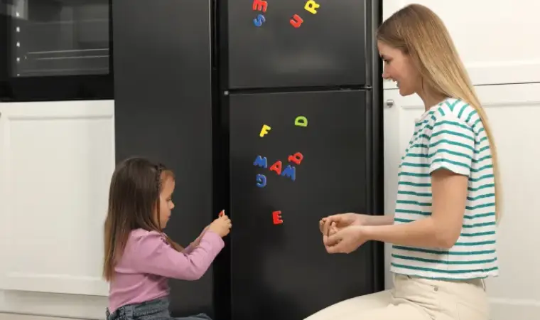 Mãe e filha colocando imãs em uma geladeira preta.