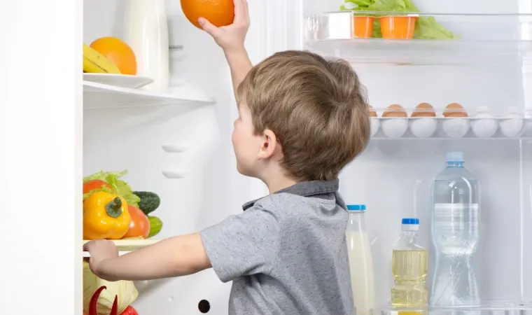 Criança colocando uma fruta dentro da geladeira pequena.