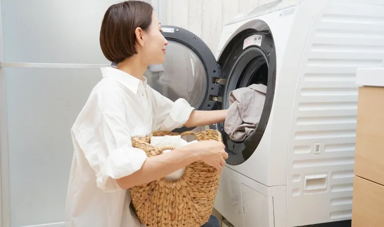 Mulher colocando roupas dentro do tambor de uma lavadora com abertura frontal.