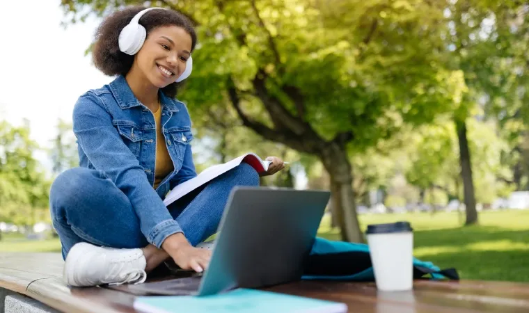 Imagem mostra uma moça sentada em uma praça usando um notebook bom e barato.