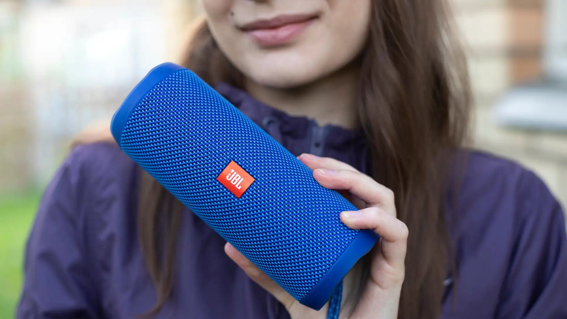 Jovem mulher segurando uma caixa de som JBL azul na mão