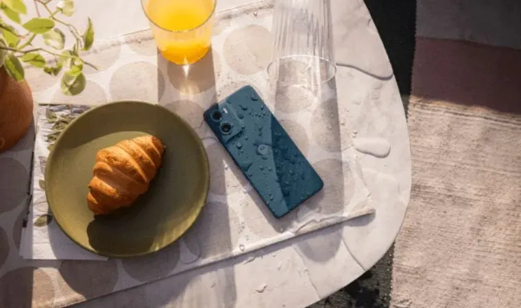 Um celular molhado está sobre uma mesa ao lado de utensílios de cozinha e um croissant