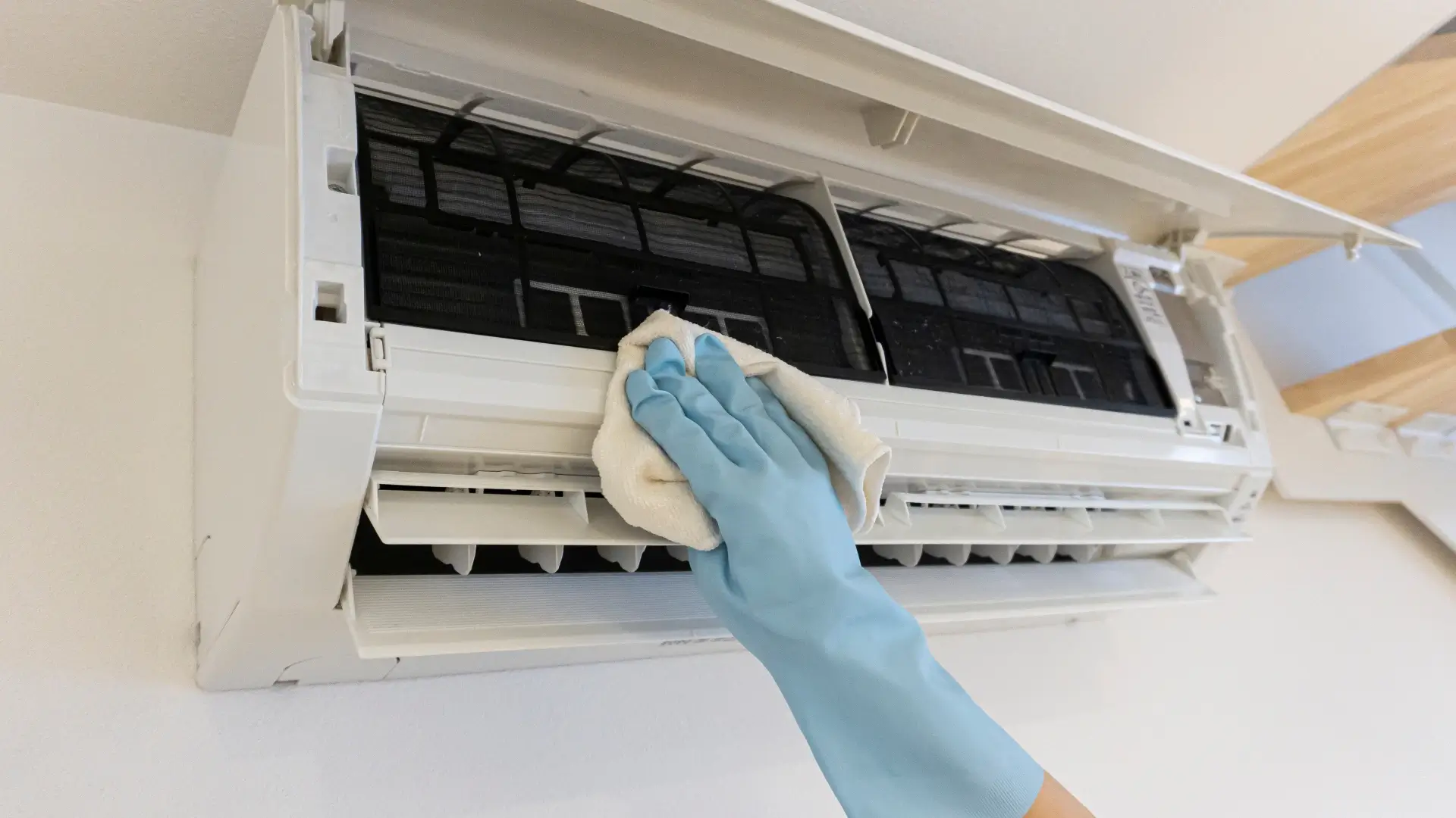 Imagem de uma mão passando um pano de limpeza em um ar-condicionado aberto 