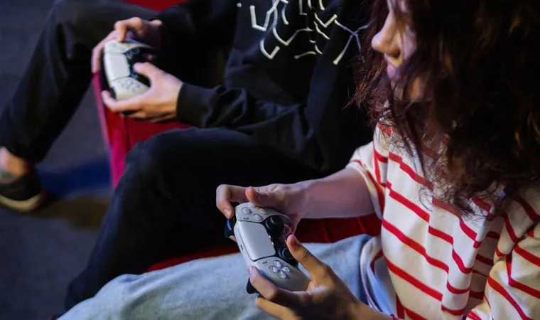 Imagem de duas crianças jogando um PlayStation 5 com controles DualSense em mãos