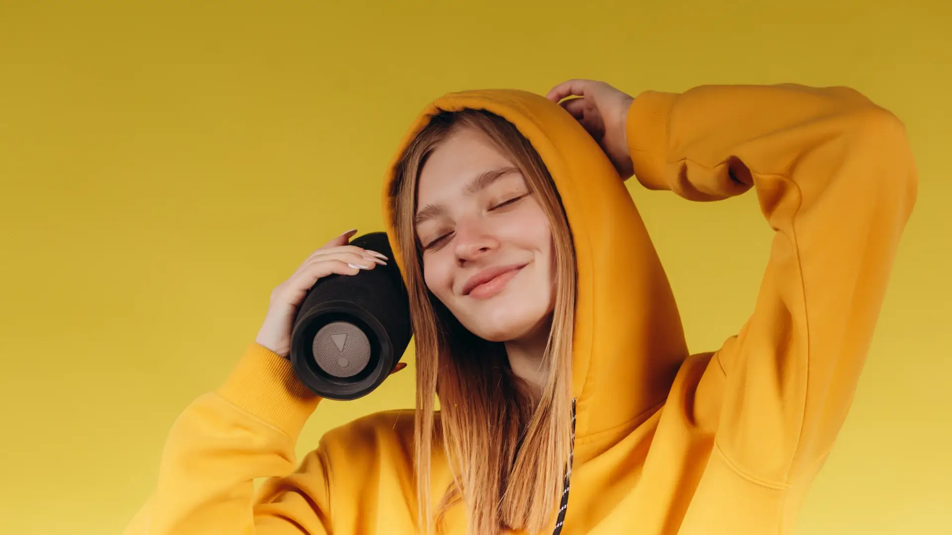 Jovem mulher de casaco amarelo segurando caixa de som  