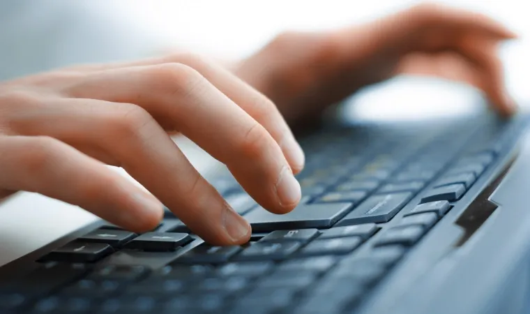 Pessoa digitando em um teclado preto sobre mesa de escritório.