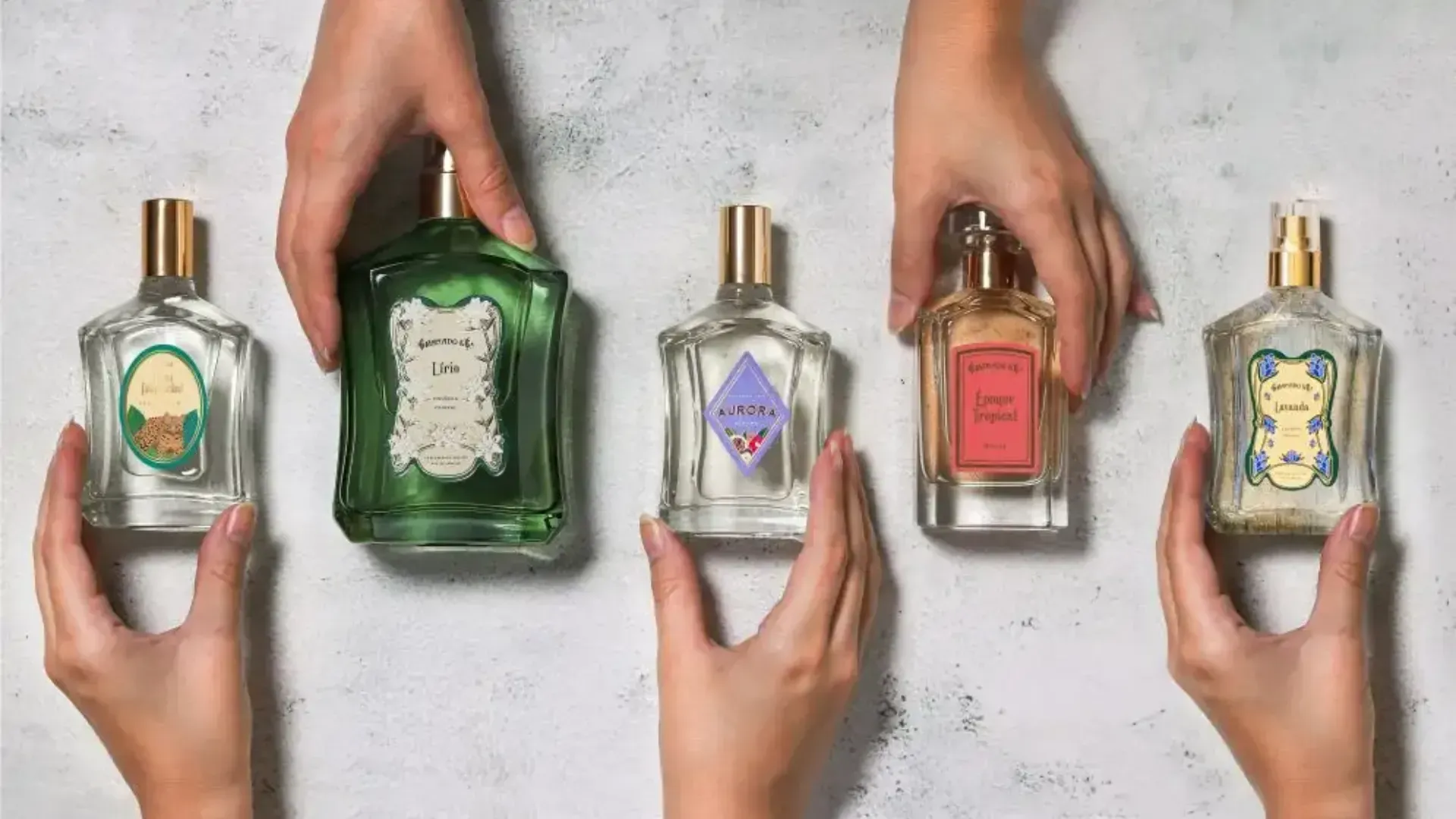Imagem de cinco mãos segurando cinco perfumes granado em cima de uma mesa de mármore