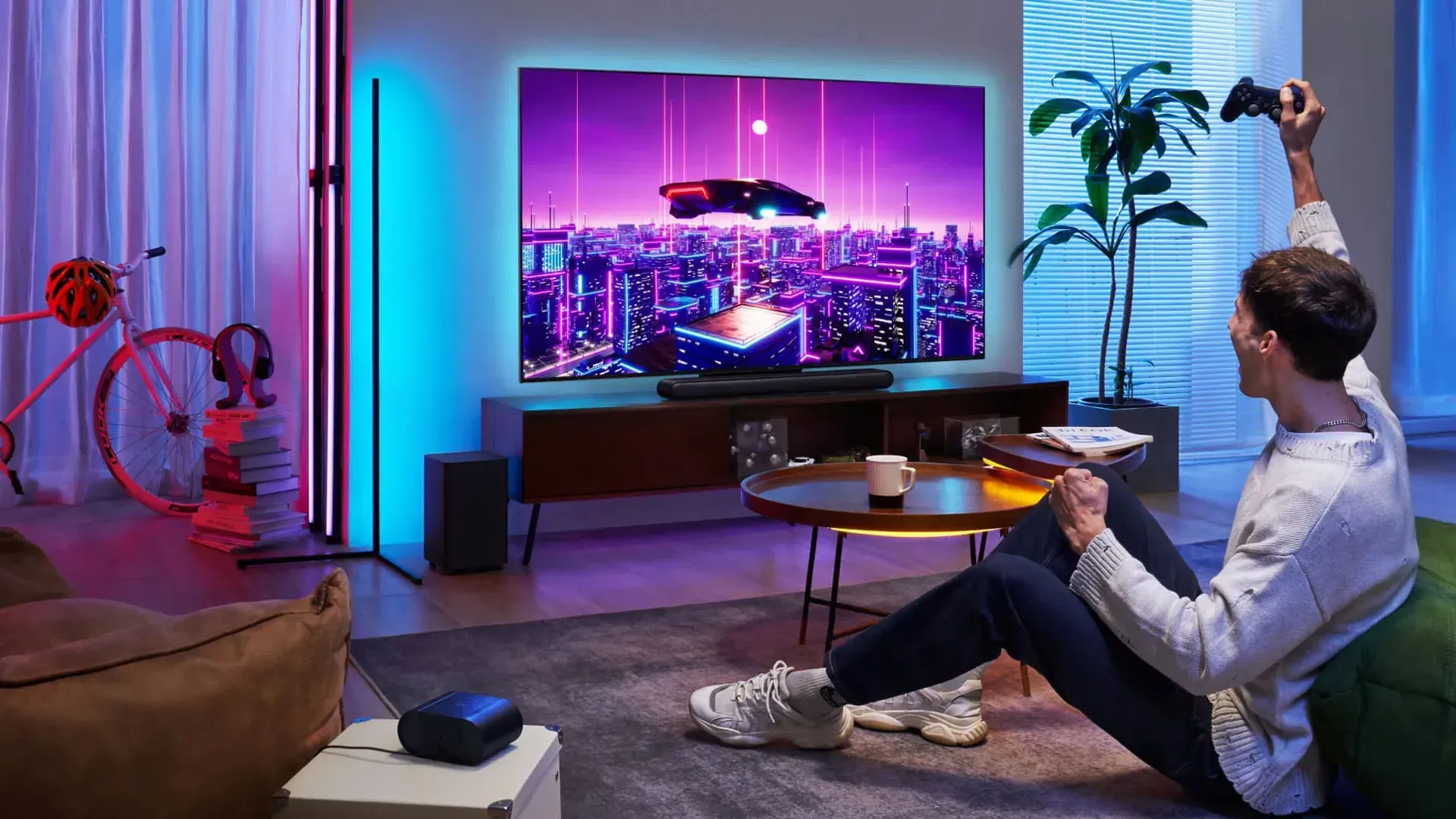 Imagem de uma pessoa jogando videogame em sala iluminada por luzes coloridas, com TV TCL C755 exibindo imagem futurista em 4K. 