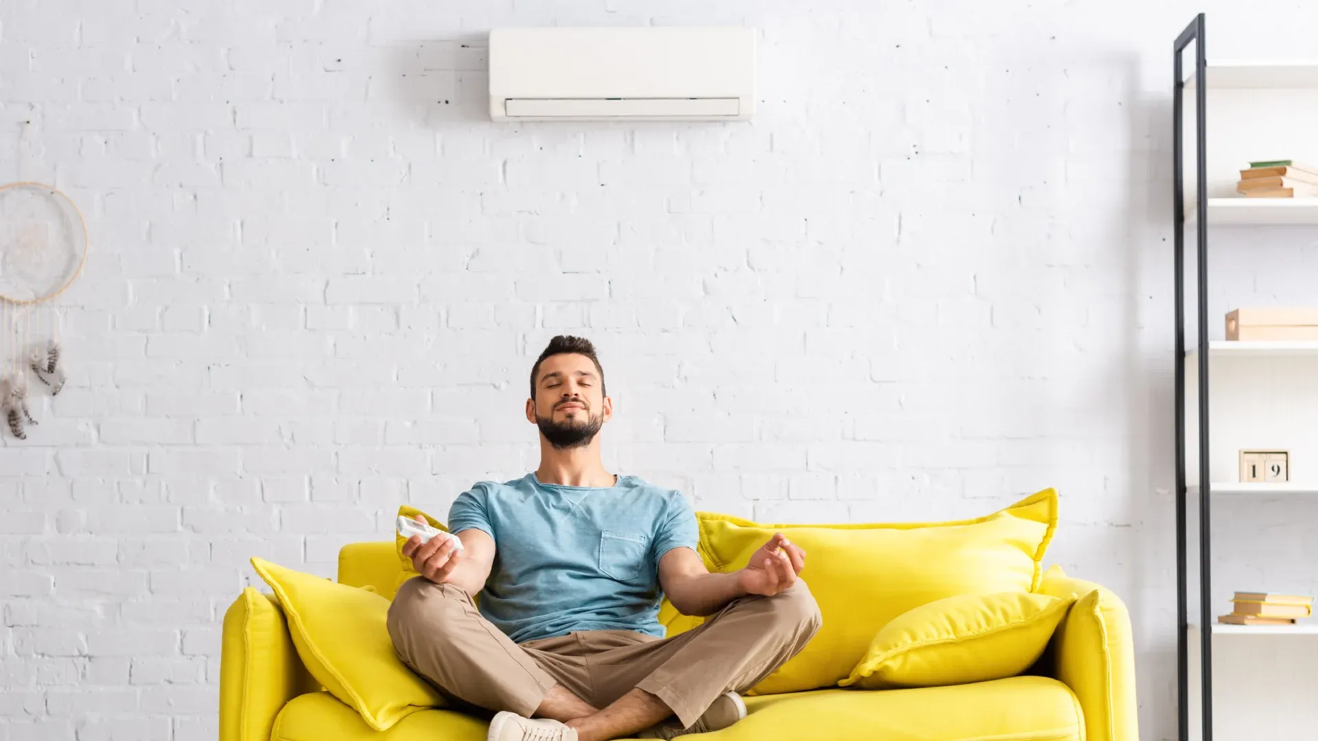 Jovem homem meditando no sofá amarelo e aproveitando o ar-condicionado