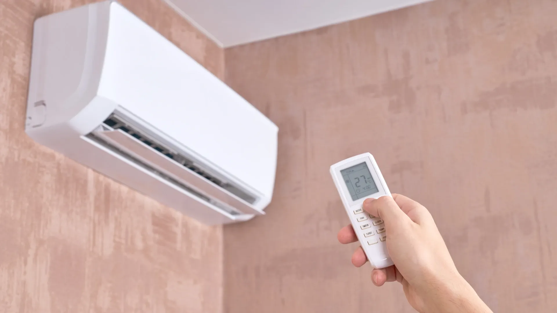 Mão segurando controle de ar-condicionado 9000 BTUs e apontando para o aparelho.