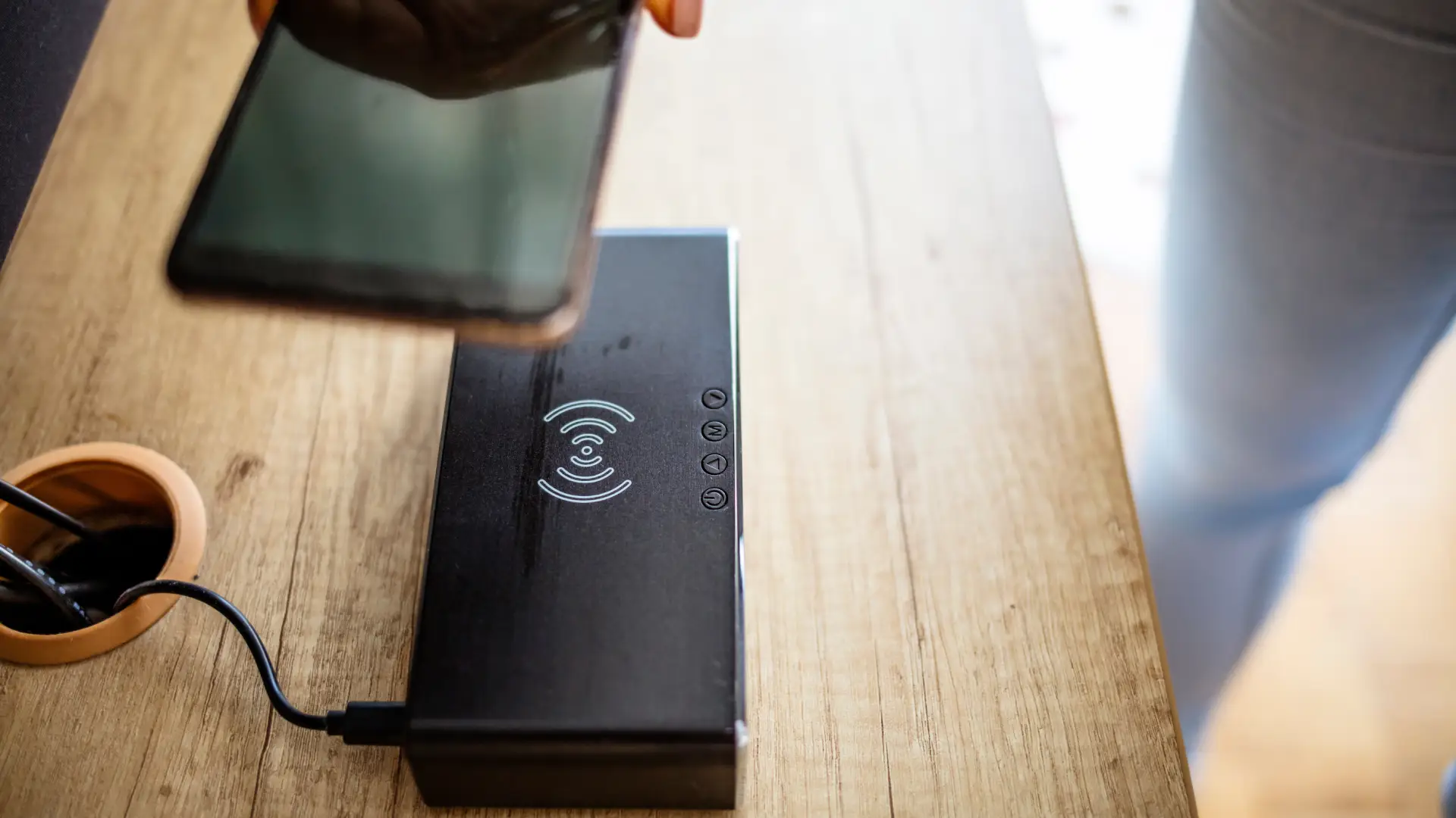 Homem levando seu celular até o carregador por indução sobre mesa de madeira