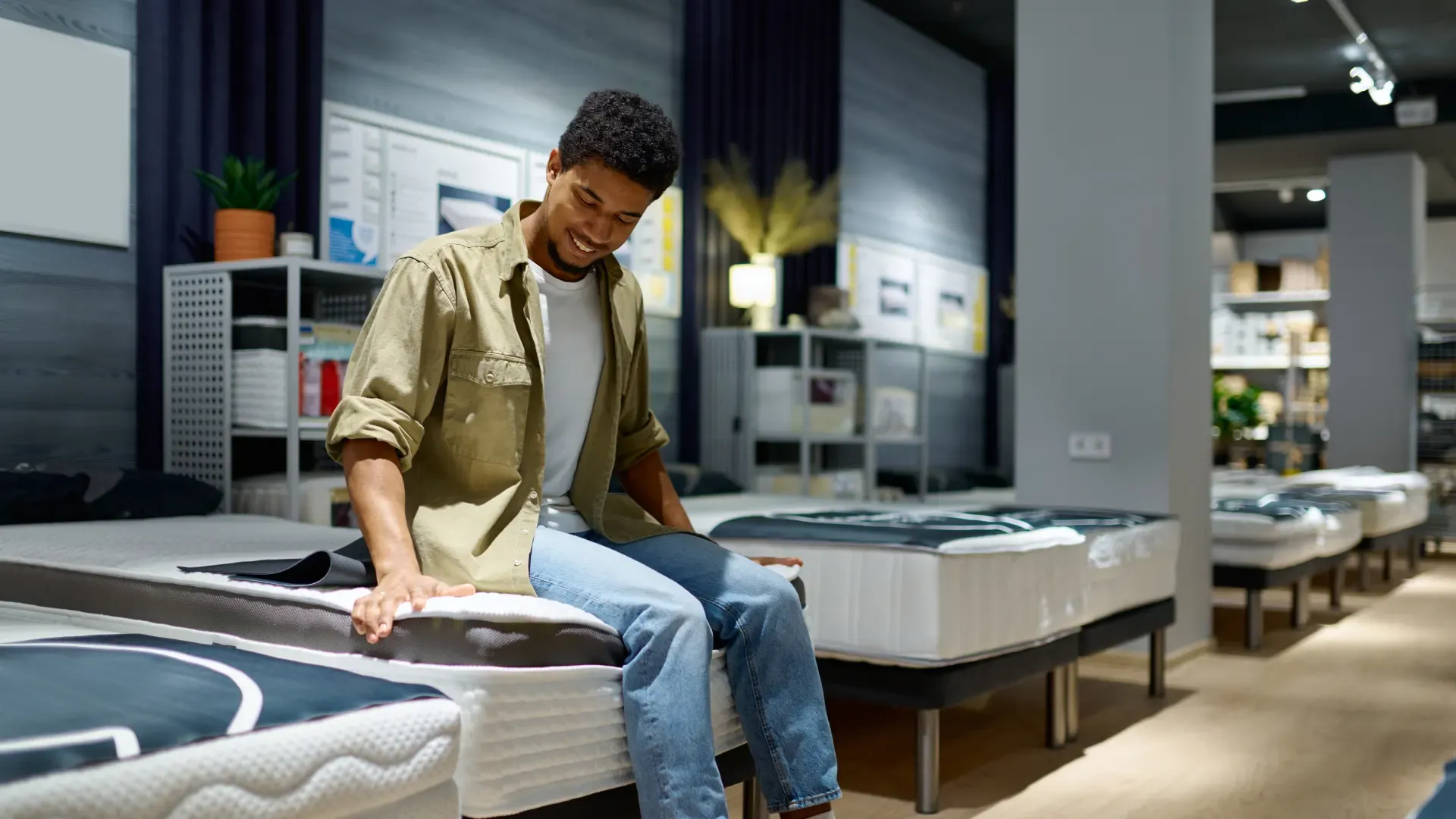 loja de colchões, homem sozinho sentado em um dos modelos de cama solteiro testando densidade do colchão