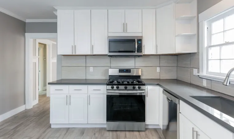 Cozinha moderna e branca com fogão de piso, bancada de granito e microondas inox