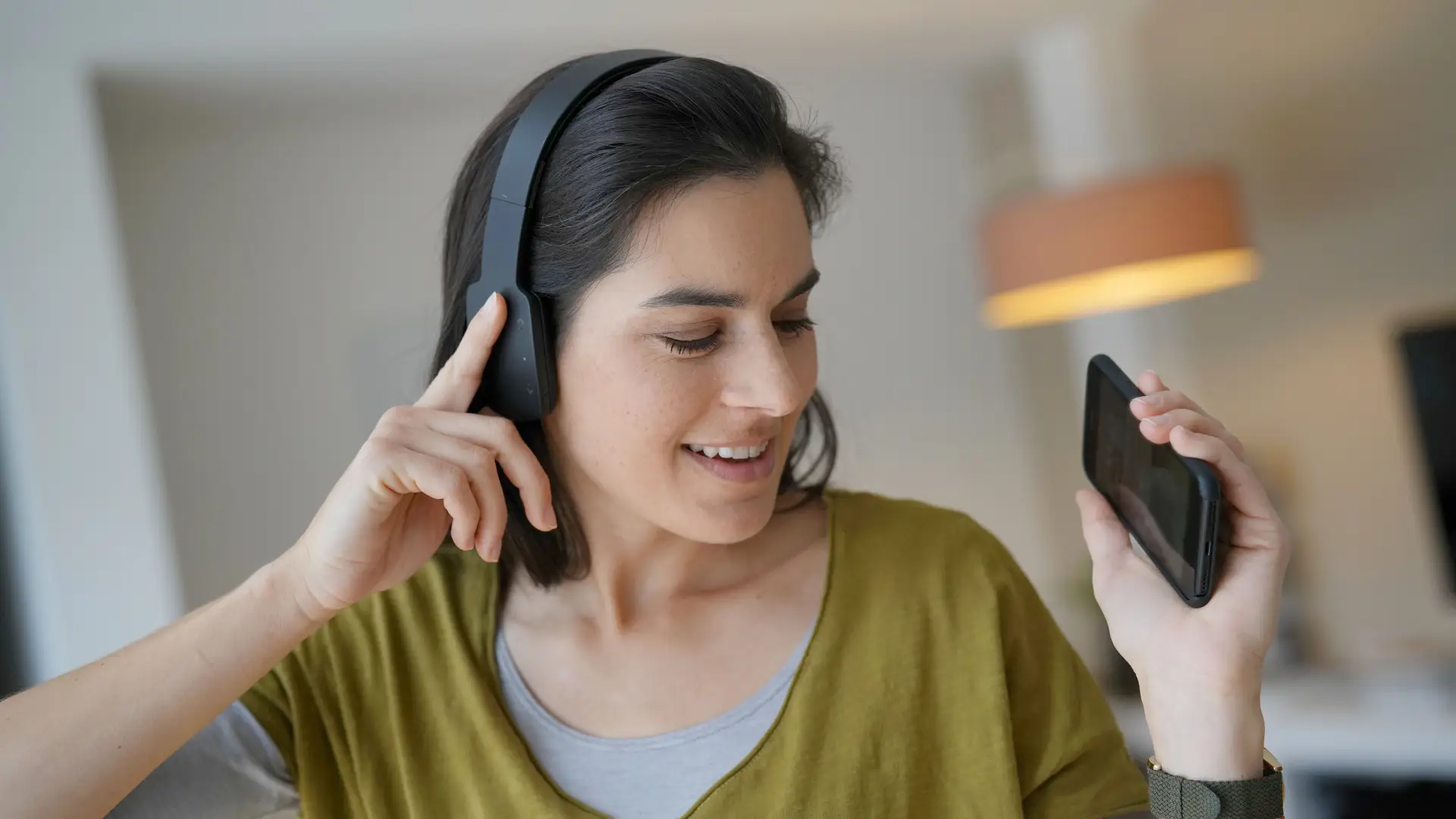 Uma mulher está com um fone de ouvido sobre a cabeça e segura um celular com uma das mãos