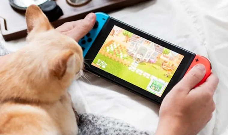 Foto do Switch em seu modo portátil sendo jogado em uma cama com um gato olhando a tela