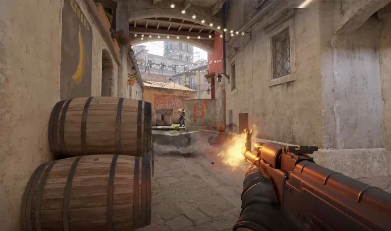 Imagem do jogo Counter-Strike 2 em primeira pessoa mostrando um rifle sendo disparado em direção a um adversário em meio a um apertado corredor com barris à esquerda 