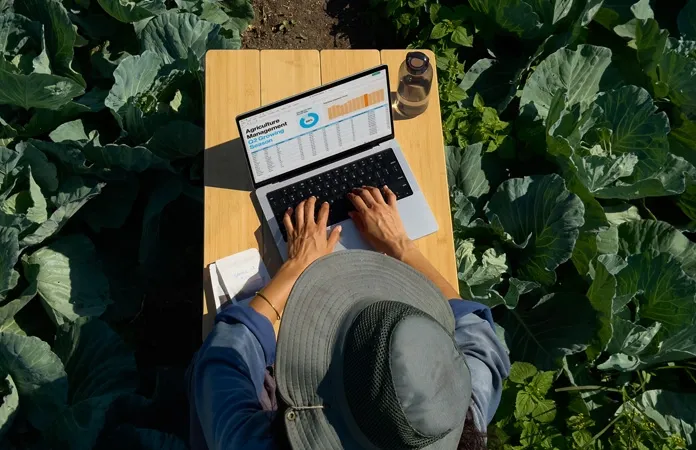 Homem ao ar livre em meio a plantação usa Macbook Pro M5 sobre mesa de madeira