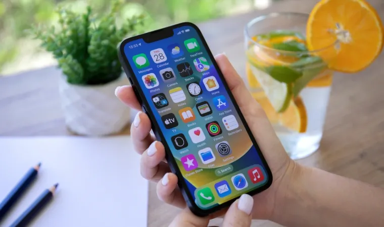 Imagem de uma mão segurando o iPhone 13 com a tela ligada e vários apps sendo mostrados