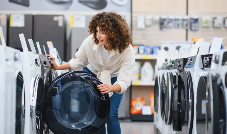 Mulher escolhendo uma máquina de lavar para comprar em meio a vários modelos.