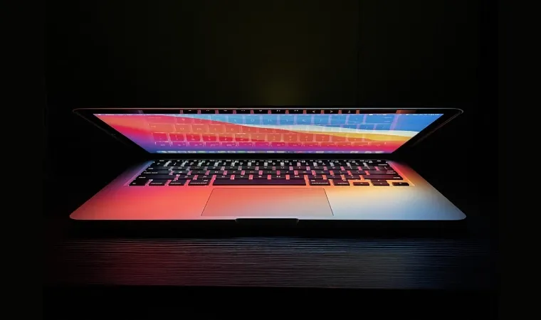 Imagem de um MacBook semiaberto em um cenário com fundo todo preto